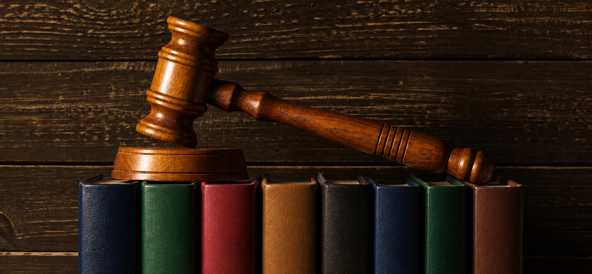 A wooden judge's gavel resting on a row of colorful law books against a dark wooden wall, representing an aggravated assault lawyer preparing a criminal defense.