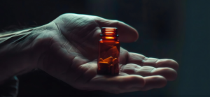 A close up of a hand holding a small amber prescription pill bottle with capsules, representing drug possession and drug offence legal matters.