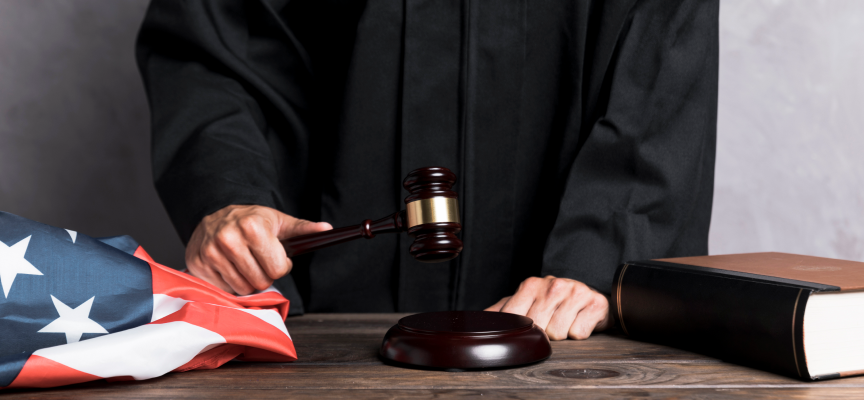 Judge in black robes holding a wooden gavel over a sound block next to a legal book, illustrating factors determining an attempted murder sentence in Canada.
