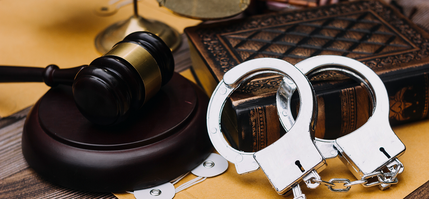Steel handcuffs resting on an antique law book beside a wooden judge's gavel, representing criminal appeals services by Edmonton lawyer Daryl Royer.